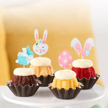Decorated table with colored eggs, flowers and assorted flavor Bundtinis with easter eggs and bunnies toppers.