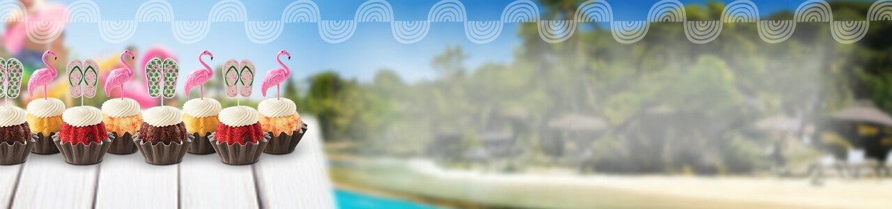 Bundtinis with flamingo and sunglasses toppers on a table poolside.