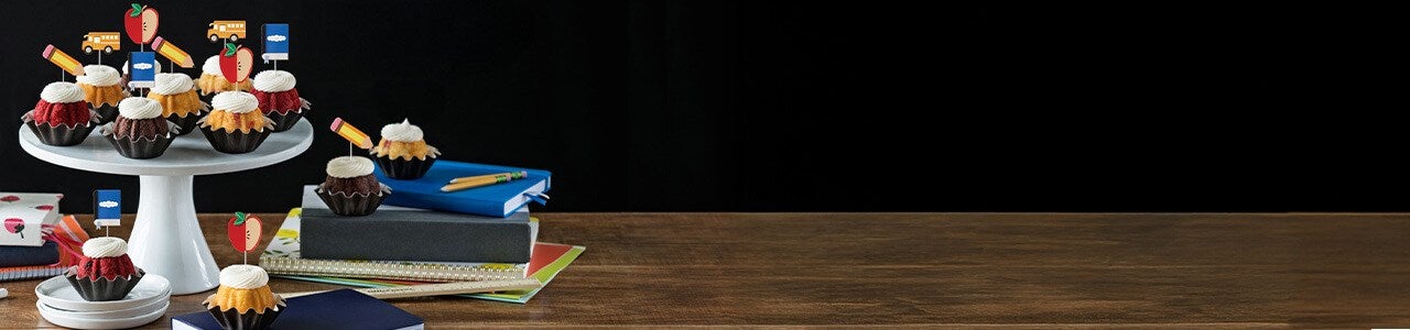 Bundtinis with pencil, notebook, red apple, and yellow bus toppers on a table.