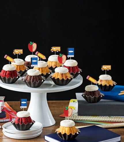 Bundtinis with pencil, notebook, red apple, and yellow bus toppers on a table.