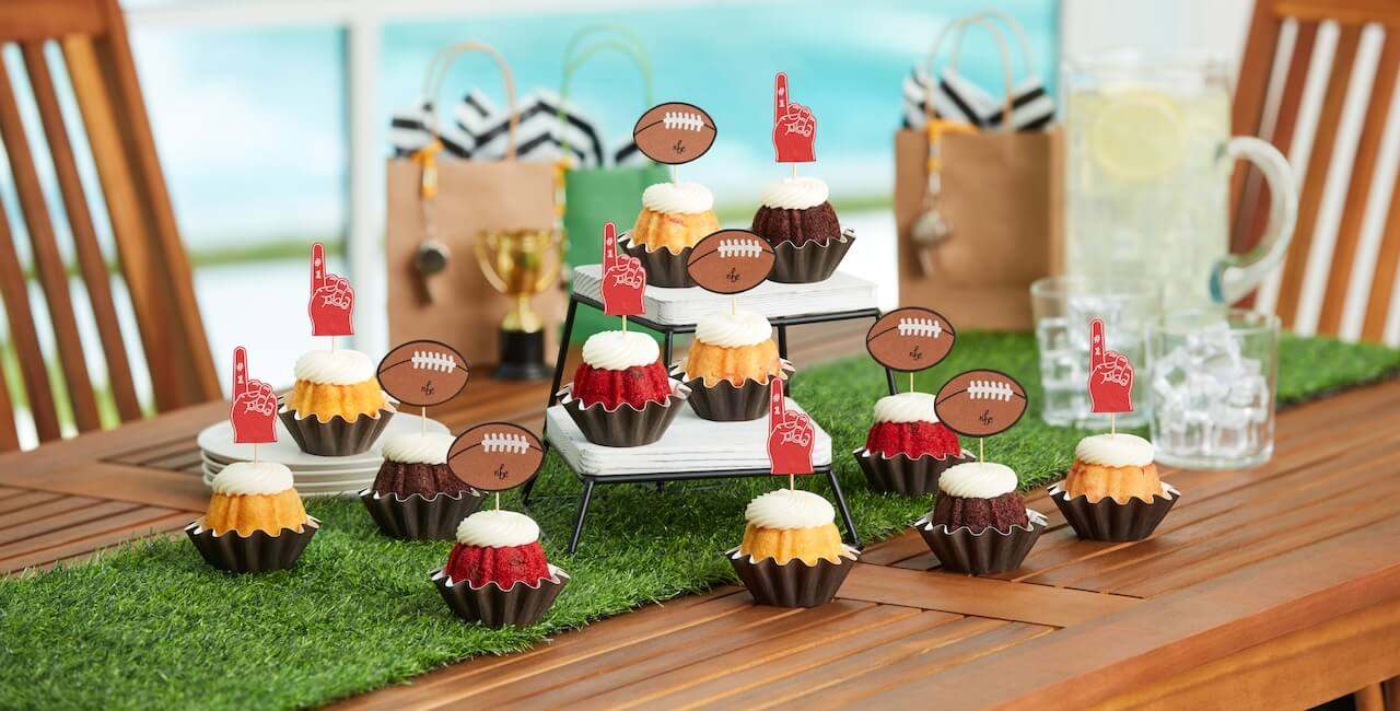Mini bundt cakes decorated with football and foam finger toppers, displayed on a grass-themed table setup.