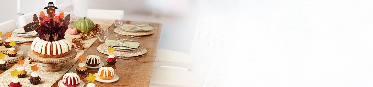 Assorted bundtinis and a bundt cake with holographic ghosts, black cat cutouts and boo sign decorations.