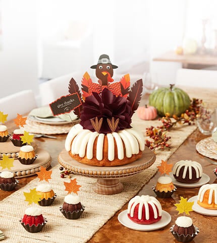 Assorted bundtinis and a bundt cake with holographic ghosts, black cat cutouts and boo sign decorations.