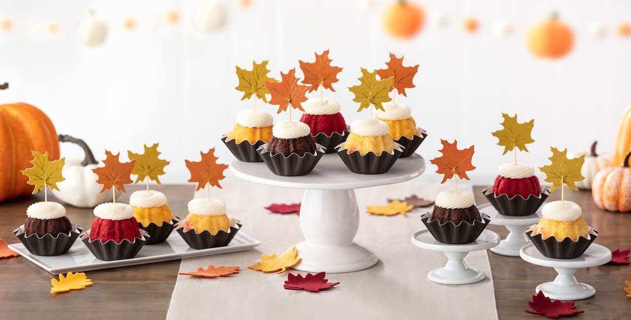 Assorted bundt bundtinis with cream cheese frosting, displayed with fall leaves decorations.