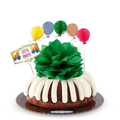 Bundt Cake with signature frosting decorated with green paper bow, assorted color paper ballons, and quote card.