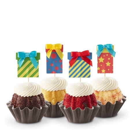 Four birthday Bundtinis in variety of flavors with cream cheese frosting and colorful gift box toppers with ribbons and bows