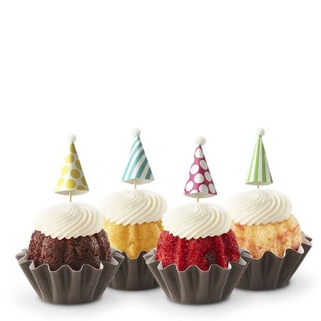 Four birthday Bundtinis in variety of flavors with cream cheese frosting and colorful party hat toppers with stripes and polka dots.