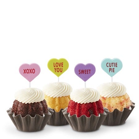 Four Valentine's Day Bundtinis in variety of flavors with cream cheese frosting and conversation heart toppers with romantic messages.