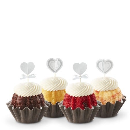 Four Bundtinis in variety of flavors with cream cheese frosting and white heart toppers for Valentine's Day or romantic occasions.