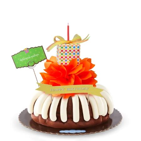 Delicious Wishes Bundt Cake with cream cheese frosting, orange tissue paper flower, polka dot gift box with candle, Happy Birthday banner, and Delicious Wishes sign for birthday celebrations.