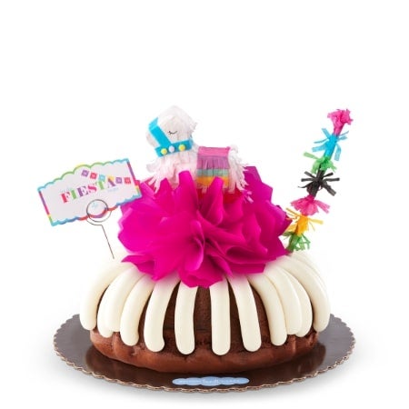 Let the Fiesta Begin Bundt Cake with cream cheese frosting, large pink tissue paper flower, colorful papel picado banners, a piñata in the center and a Let the Fiesta Begin sign for birthdays.