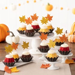 Cupcake-sized mini cakes with frosting and decorated with fall leaves toppers. 