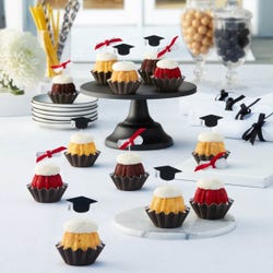 Cupcake-sized bundt cakes adorned with small toppers with a black graduation cap and  a diploma tied with a red ribbon