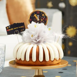 A bundt cake with a celebratory bow in the center with gold and silver stars. It contains a countdown clock topper and a card that reads Hello New Year.