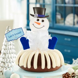 A decorated bundt cake with a snowman with a carrot nose and 2 knit mittens. A card is on the cake that says Let It Snow!.