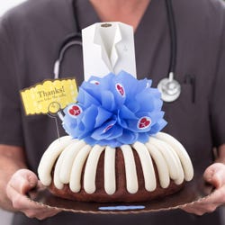 A decorated bundt cake with frosting. The center includes a blue bow with heartbeat stickers and a white lab coat and a card that reads Thanks! You take the cake.