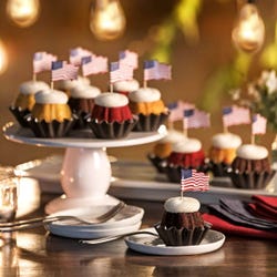 Mini Bundt cakes (Bundtinis®) in a row with creamy white frosting. Each Bundtini is topped with a small American flag.
