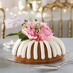 Bundt cake decorated with a beautiful pink flower arrangement with greenery. A card reads yours