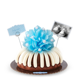 A bundt cake with a blue bow in the center with a small photo card of baby shoes and a blue dotted card that reads baby cakes. Sweet congratulations!. 