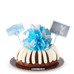 A bundt cake topped with a blue bow and adorned with soft white wings. 