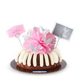 A bundt cake topped with a pink bow and adorned with soft white wings. 