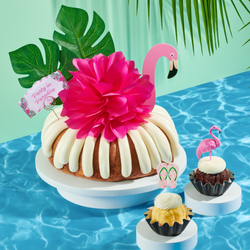A bundt cake decorated with a pink flamingo with tropical leaves. It also includes a card that reads Party in Paradise. 
